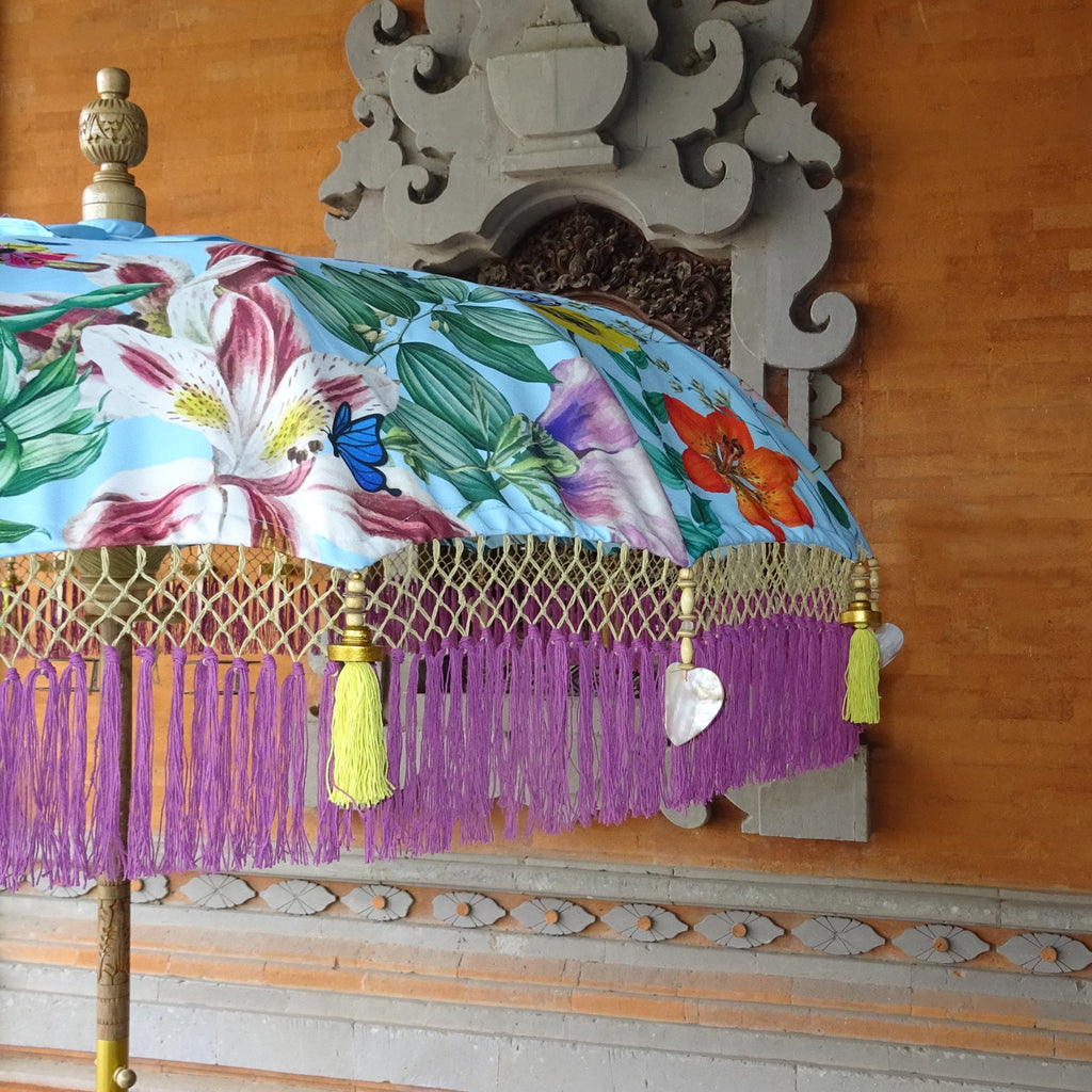 Top view of the Butterfly Parasol, a Balinese handmade umbrella with a sky-blue canopy decorated with colorful butterflies and exotic flowers.
