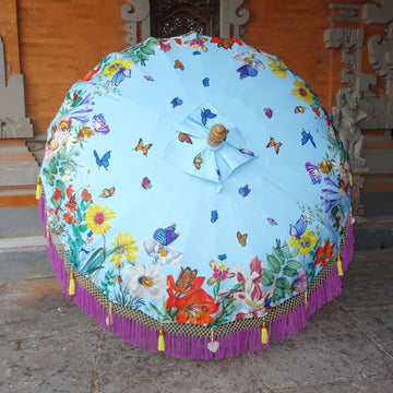 Close-up of the Butterfly Parasol’s canopy, showcasing vibrant floral patterns, blue butterflies, lilac fringe, golden tassels, and mother-of-pearl shell accents.