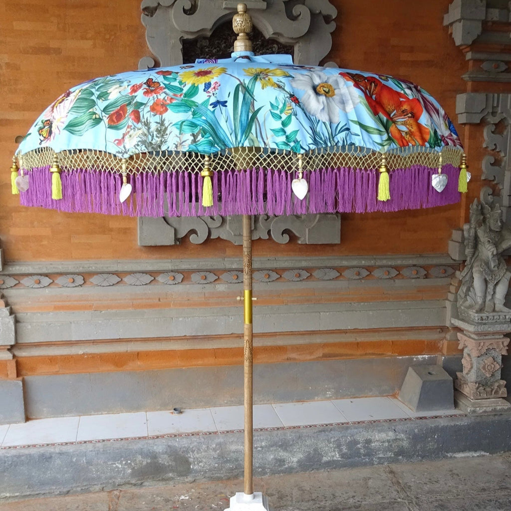 Full view of the Butterfly Parasol, a handcrafted Balinese umbrella featuring a floral and butterfly design, a hand-carved wooden pole, and elegant lilac fringe.