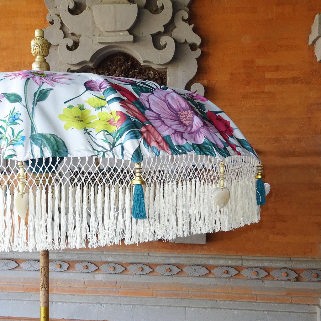 Close-up of Daisy Parasol’s intricate floral patterns in pink, purple, and yellow with white fringe and green tassels.